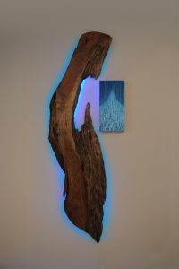 wall sculpture with piece of wood backlit with blue light and a small painted panel next to it