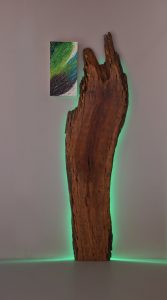 sculpture with salvaged wood backlit with green light and a small painted panel next to it