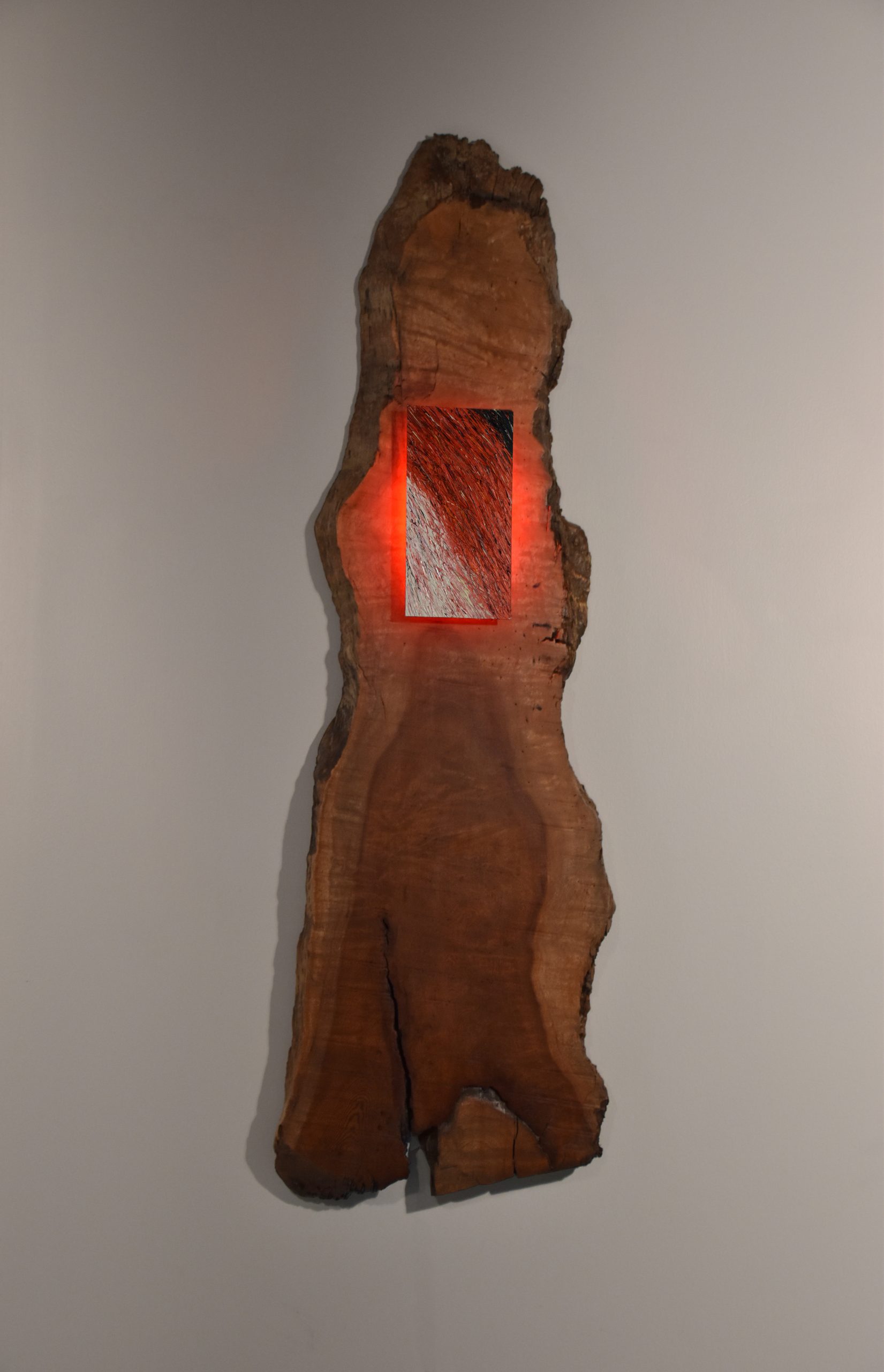 sculpture with salvaged wood and a small painted panel on it which is backlit with red light