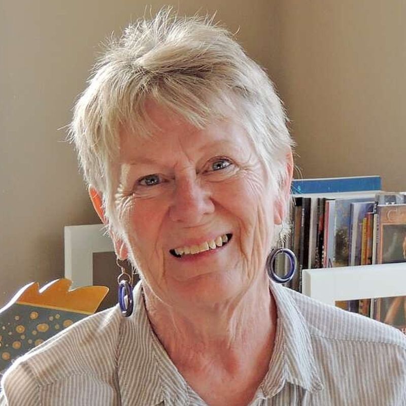 A white woman with short hair, wearing a button up shirt indoors.