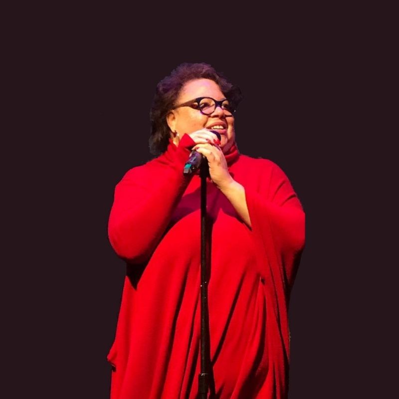 A black woman in a red dress, standing at a microphone.