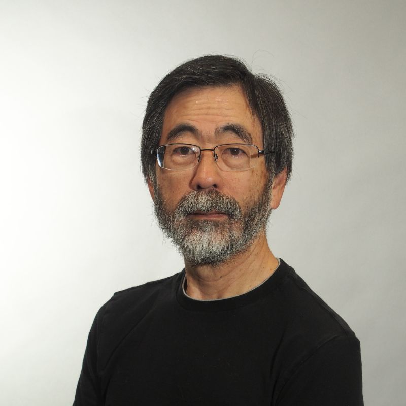 A headshot of an Asian man with glasses and a beard in a black sweater, in front of a white background.
