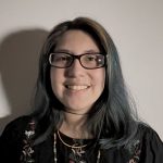 A woman wearing glasses amd a black shirt, with many beaded necklaces on.