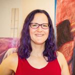 A white woman in a red shirt, next to a large painting that looks like her.