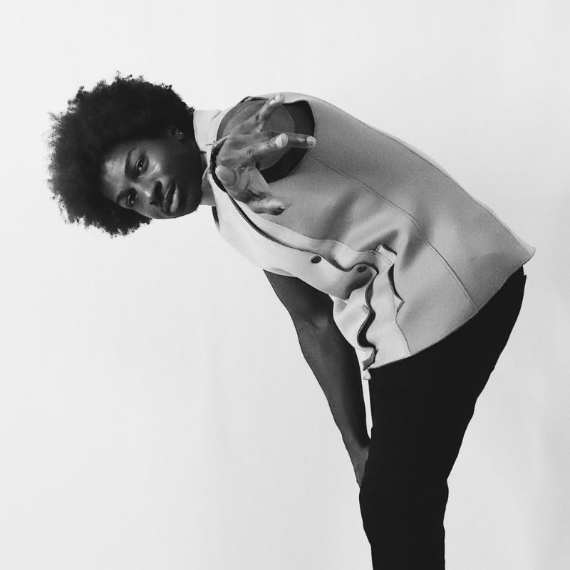 A black and white photo of a black person in front of a white backdrop, bending over.