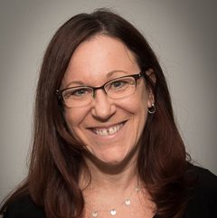 A woman with a black and blue shirt and glasses against a gray background.
