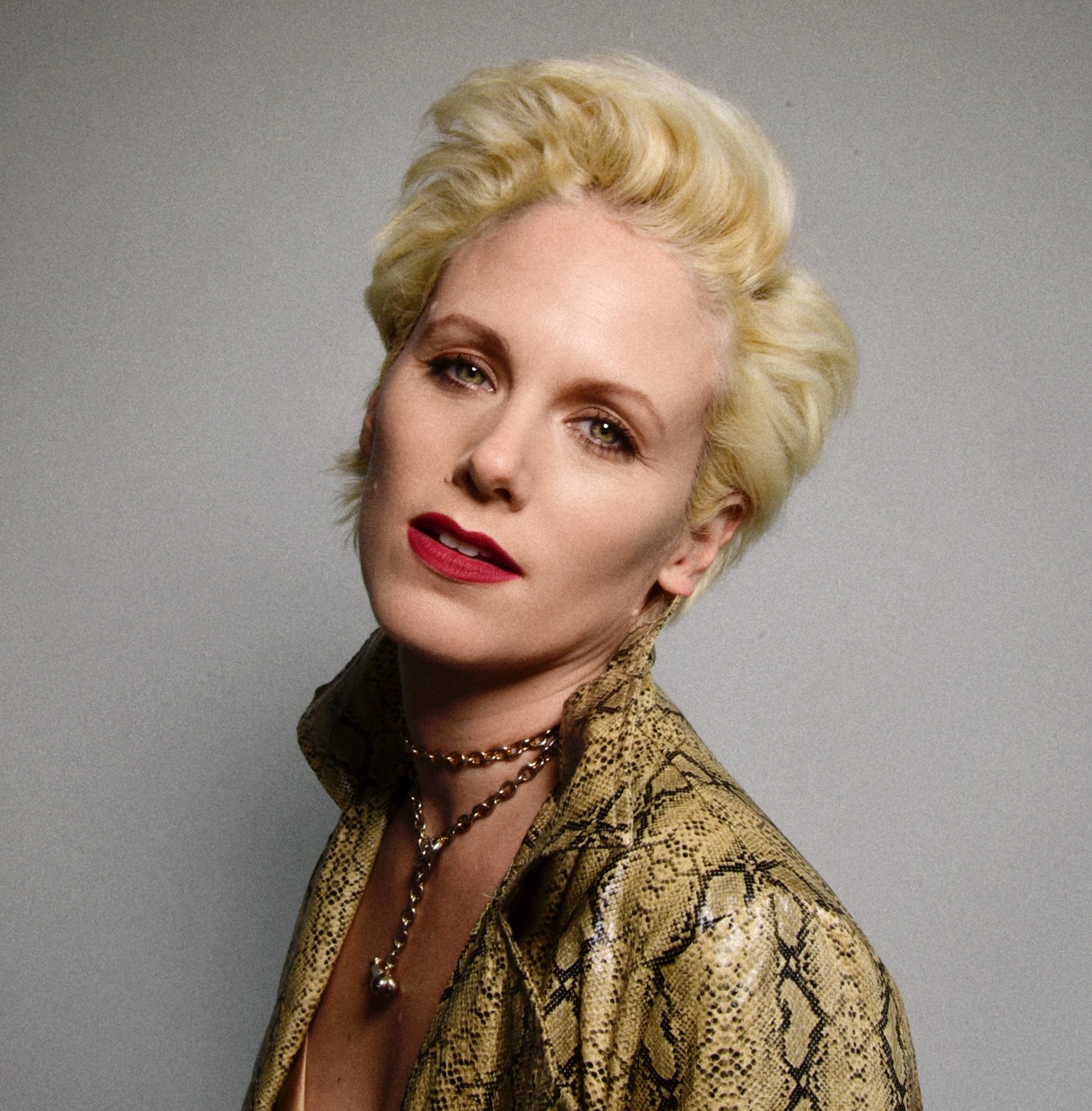IVA Headshot - a woman with blonde hair and a gold shirt against a gray wall