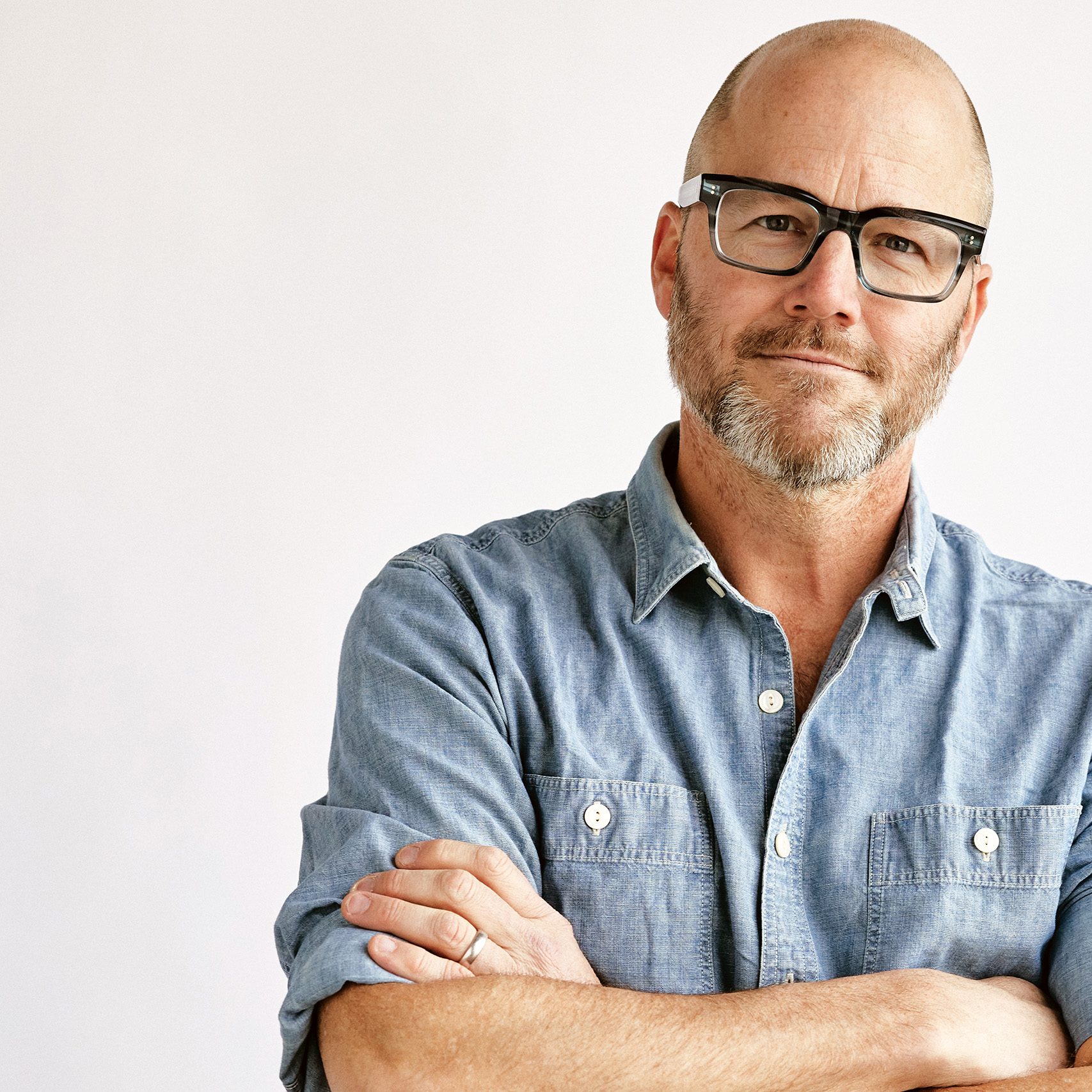 A man with a blue shirt and glasses against a gray background