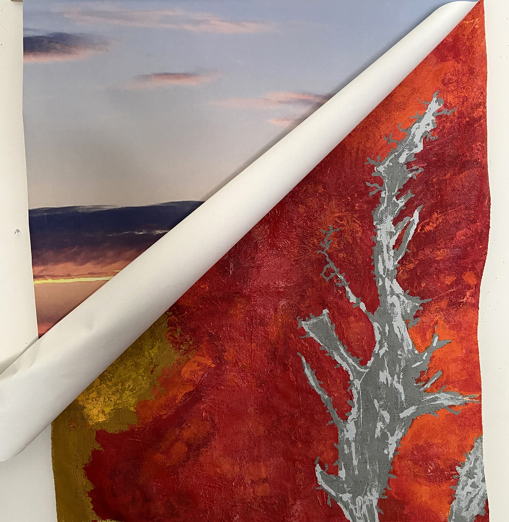 A photograph of a sunset, with paper over top rolling down revealing it. The top paper is a red painting of a heat map.