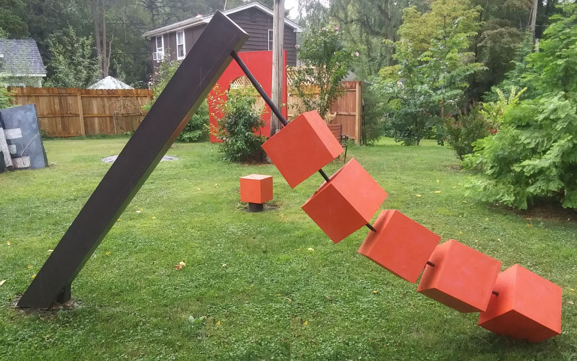 A diagonal, rectangular pole coming from the ground on grass, with large red blocks stringing along, sloping downwards.