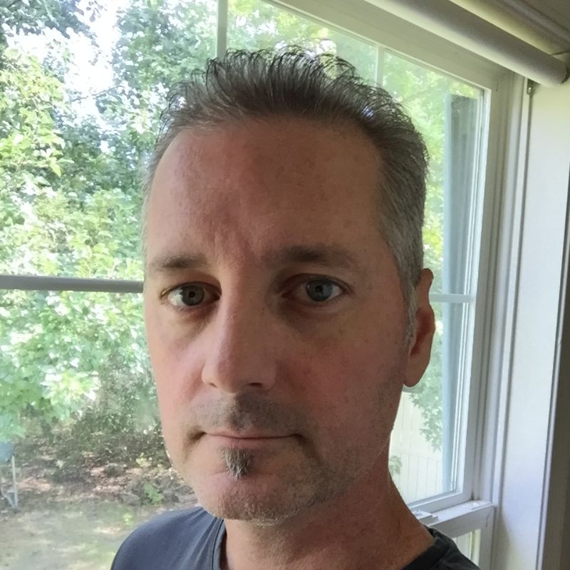 A white man with a goatee in front of a window during the day.