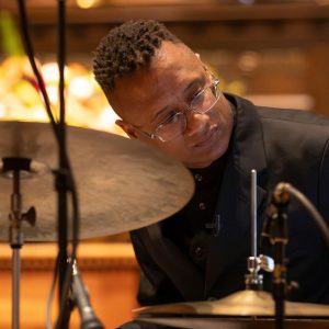 A black man in a black suit playing the drums