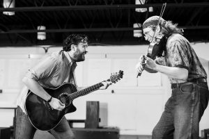 Two individuals play instruments and sing to each other.