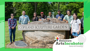 Wide promotional banner framed in green showing a group of eight people standing outdoors behind a large stone sign that reads “Copeland Sculpture Garden.” A grassy lawn and leafy trees fill the background. Bottom right includes the “Delaware Arts Incubator” logo with the tagline “Equity and Innovation.”