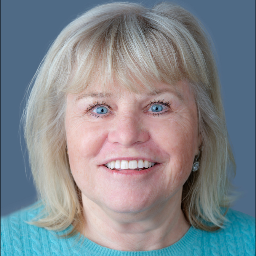 Headshot of a smiling woman with light blonde hair and blue eyes wearing a teal sweater against a blue-gray background.