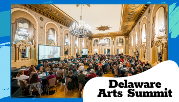 A wide photo shows a packed conference-style gathering seated at round tables in an elegant, gold-trimmed ballroom with large chandeliers and tall arched windows. A presentation screen is visible at the front. The image is framed with blue accents and a white rounded shape in the lower right that reads “Delaware Arts Summit.”