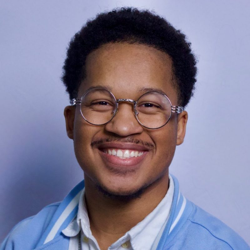 A young black man with black hair and glasses.