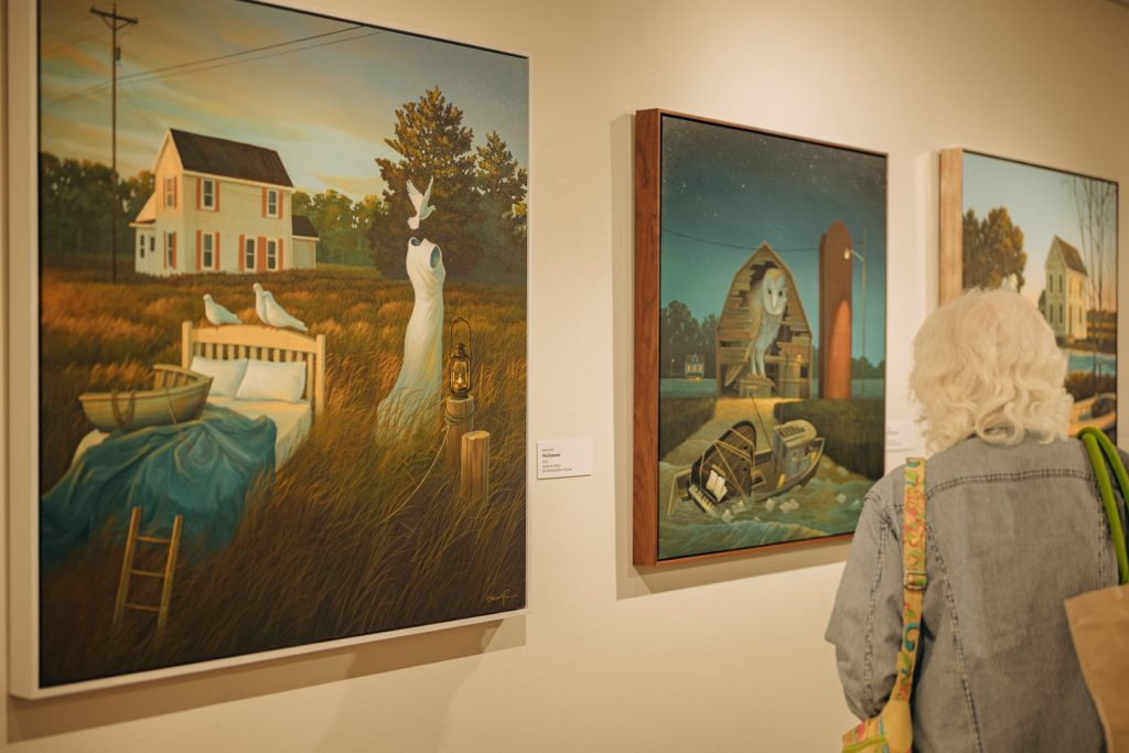 A woman stands and observes three paintings on a wall