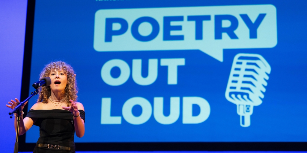 a young woman in a black shirt recites into a microphone in front of a blue poetry out loud background