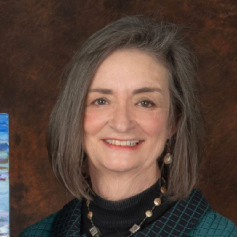 A white woman with a bob haircut, in front of a brown wallpaper.