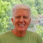 A white man with gray hair, smiling, wearing a green shirt.