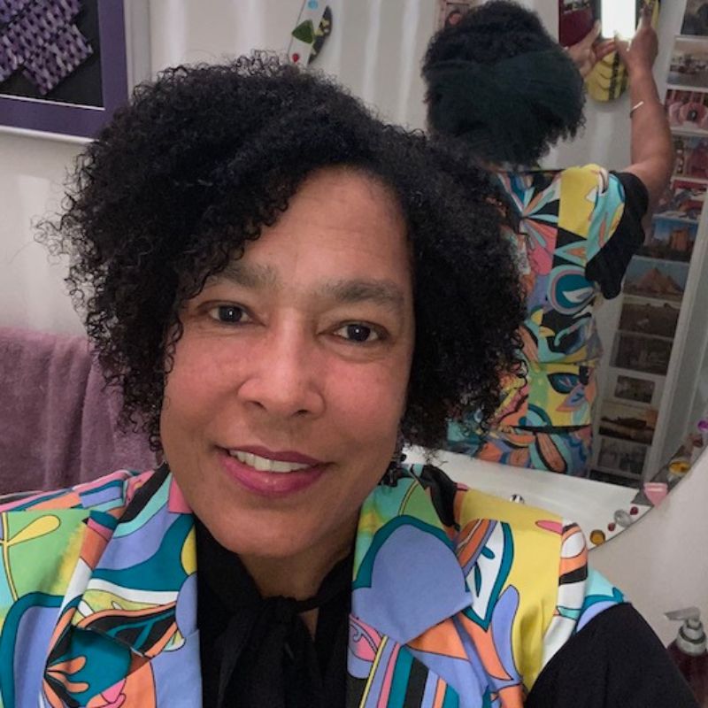 A headshot of black woman in a colorful collared shirt, indoors.