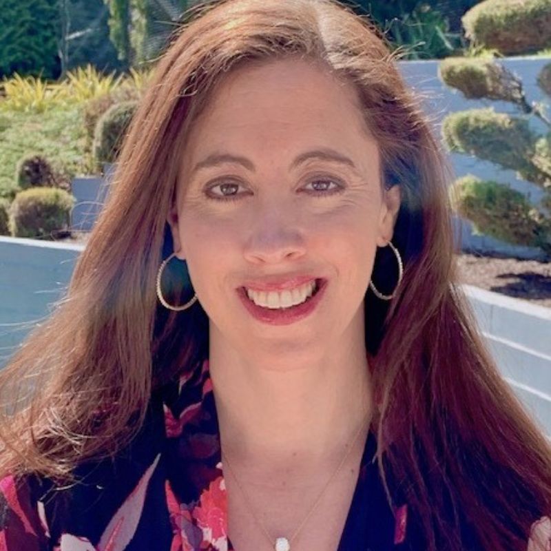 A white woman with brown hair, smiling, outside.