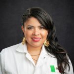 A headshot of a Mexican woman in a white button up shirt and gold earrings, with red lipstick, in front of a dark gray background.