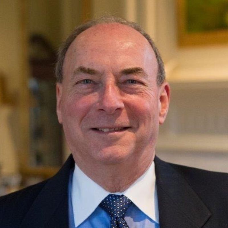 Headshot of a smiling man in a dark suit jacket with a white shirt and red tie, photographed indoors.