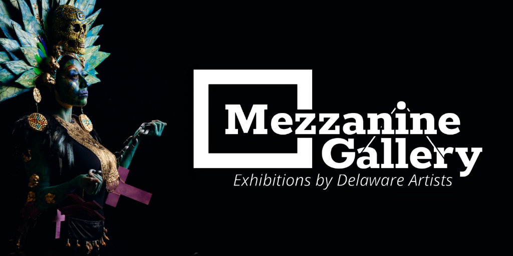 Promotional graphic for the Mezzanine Gallery featuring a dramatic portrait of a performer in elaborate blue, black, and gold costume and headdress on the left, set against a black background. The white “Mezzanine Gallery: Exhibitions by Delaware Artists” logo appears prominently on the right.